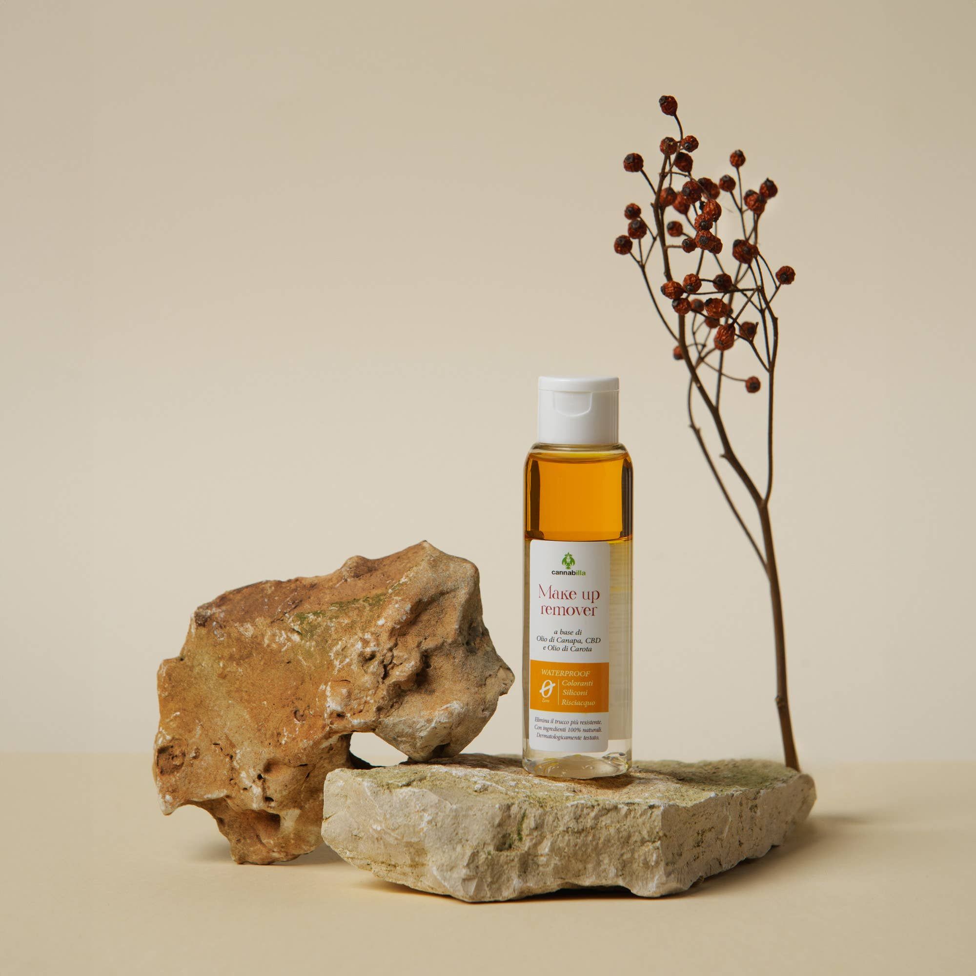 Flacone di struccante con liquido giallo. Scritta: Make up remover, a base di Olio di Canapa, CBD e Olio di Camelia. Posizionato su pietra.