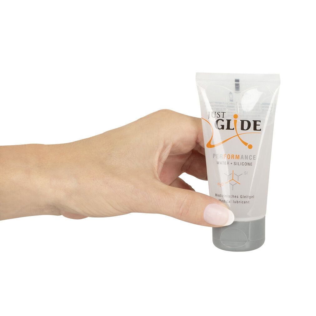 Mano che tiene un tubo trasparente con tappo grigio. Scritta: JUST GLIDE PERFORMANCE WATER + SILICONE. Testo: Lubrificante medico.