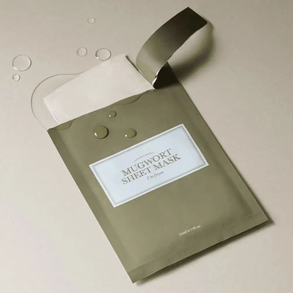 Maschera in tessuto verde aperta. Testo: MUGWORT SHEET MASK, I'm from. Accanto gocce d'acqua.