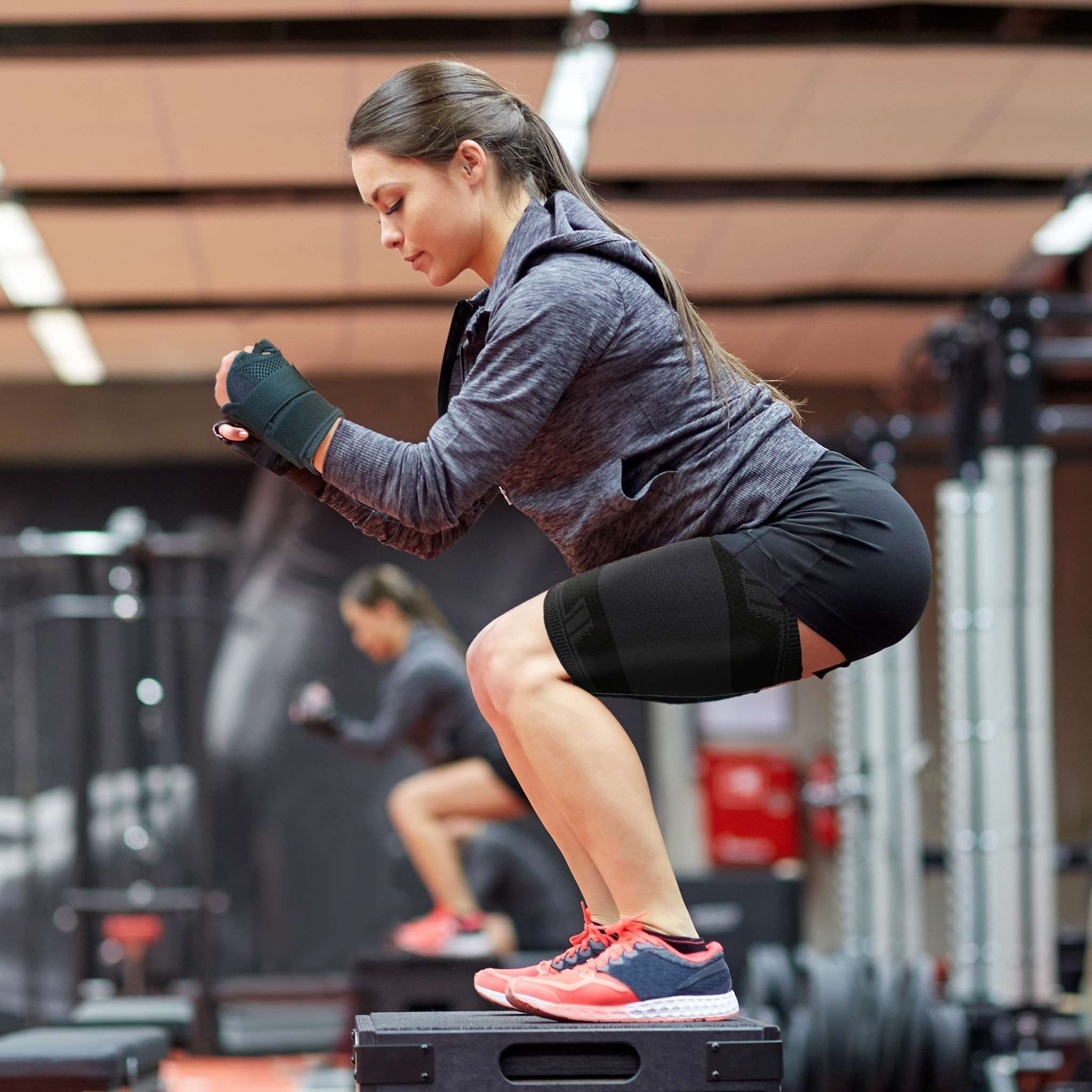 Donna che si allena con bendaggi per coscia. Fa squat su una scatola.