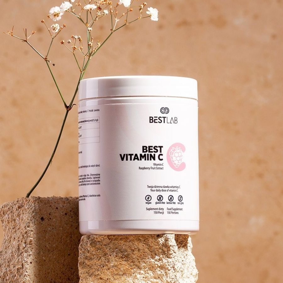 Contenitore bianco con BEST VITAMIN C. Estratto di frutta di lampone. Vegano, senza glutine, senza zucchero, senza OGM. Su un blocco di pietra.
