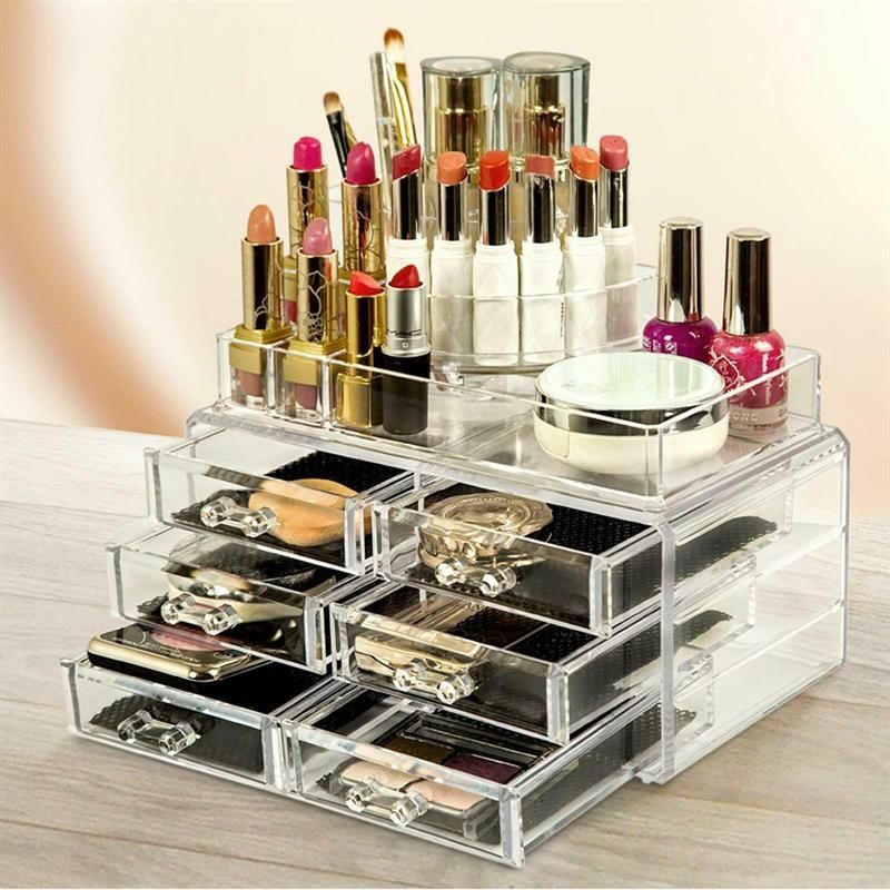 Organizzatore trucco con 6 cassetti e 18 scomparti, riempito di cosmetici. Struttura trasparente in acrilico. Fondi neri.