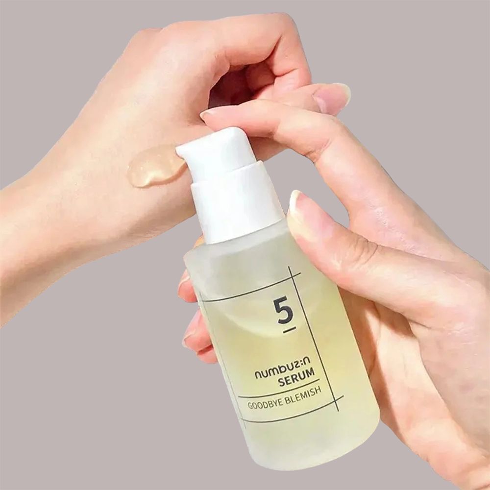 Mani che tengono un flacone di siero. Il siero viene applicato sulla mano. Scritta: 5, numbuz:n SERUM, GOODBYE BLEMISH. Liquido trasparente.