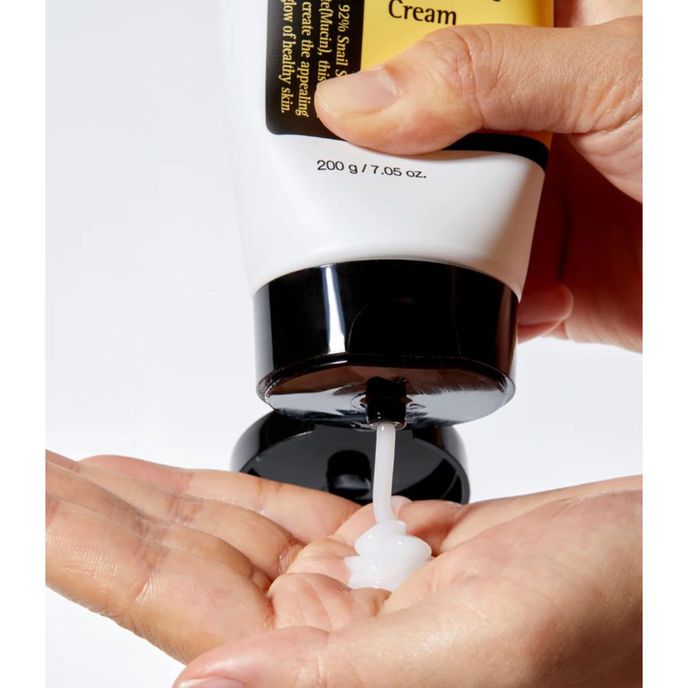 Crema spremuta da un tubetto in una mano. Tubetto: bianco, tappo nero, etichetta gialla. Testo: Advanced Snail 92 All in One Cream.