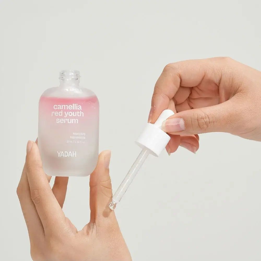 Flacone di siero con pipetta. Scritta: Camellia Red Youth Serum. Marchio YADAH. Mani che tengono flacone e pipetta.