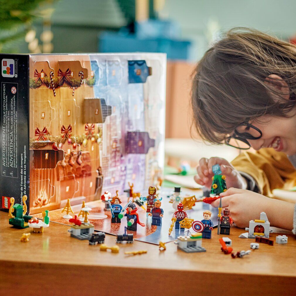Bambino che gioca con il calendario dell'Avvento LEGO Marvel. Personaggi e scene sul tavolo. Include Iron Man, Spider-Man e Captain America.