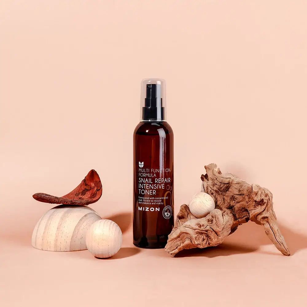 Flacone marrone con vaporizzatore, circondato da legno e decorazioni. Scritta: MIZON Snail Repair Intensive Toner.