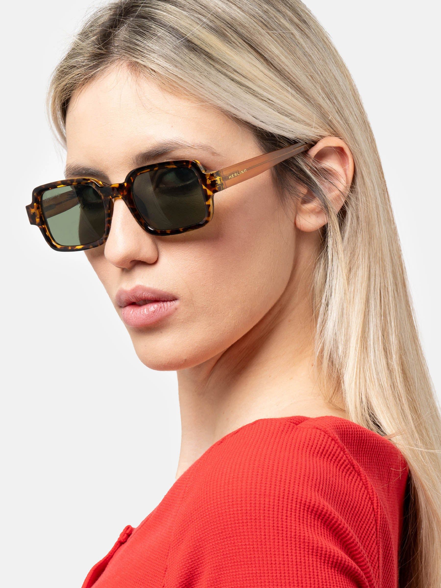 Donna con occhiali da sole rettangolari con motivo tartarugato marrone e lenti verdi. Logo Herling.