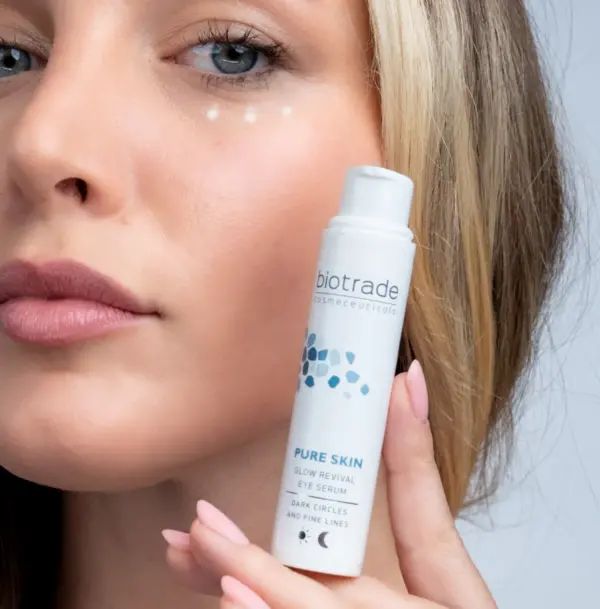 Donna tiene flacone bianco, logo Biotrade, Pure Skin Glow Revival Eye Serum, contro borse, occhiaie e rughe sottili.