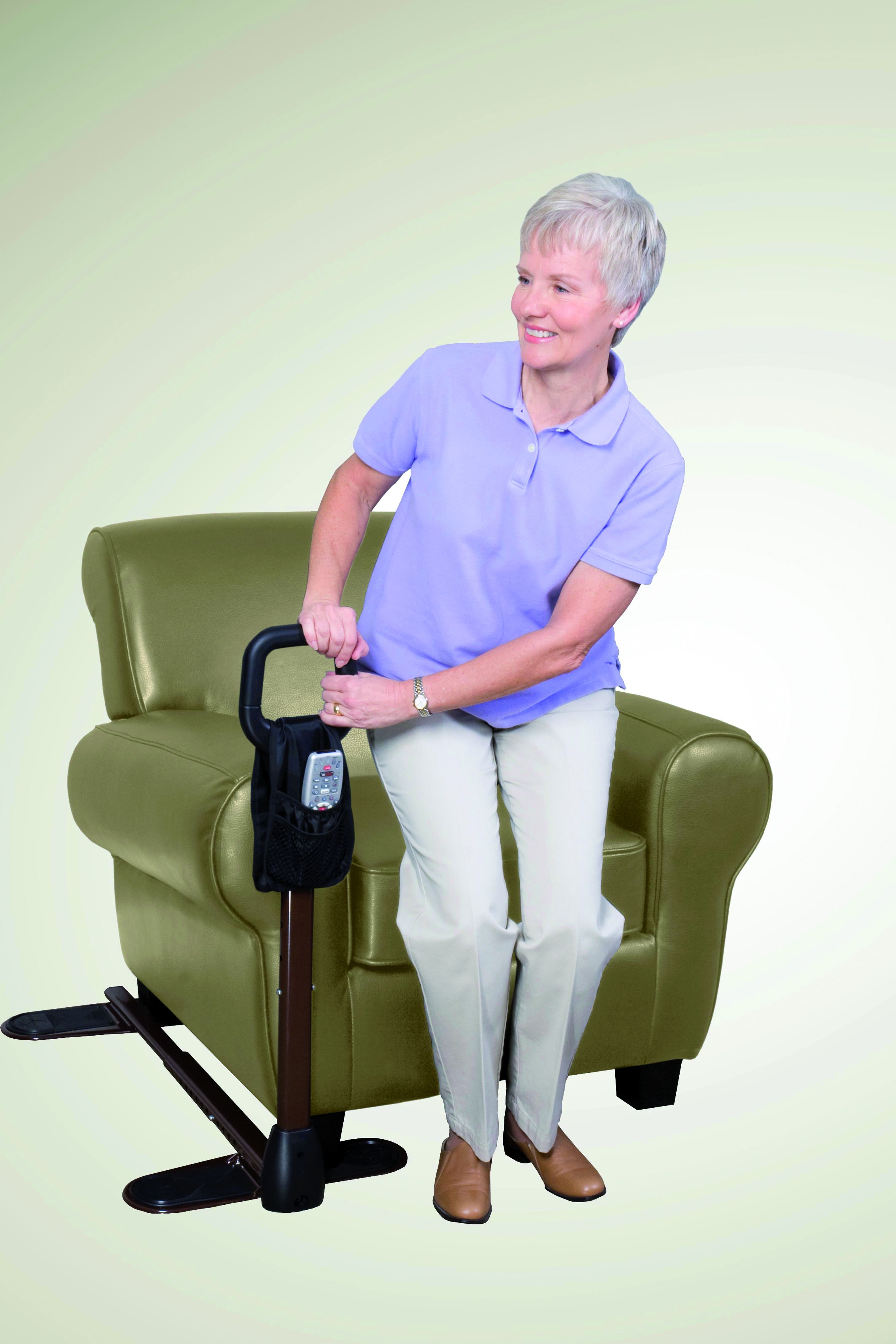 Donna usa ausilio per sollevamento accanto a poltrona verde. Maniglia nera, asta marrone, base nera. Con tasca.