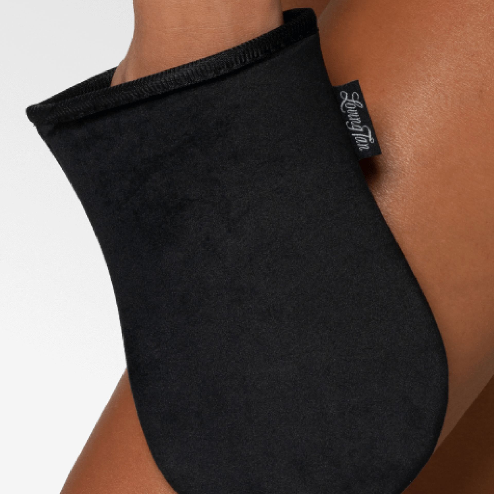 Guanto applicatore nero su una gamba. Materiale nero, etichetta con logo. Il guanto copre la mano e parte dell'avambraccio.