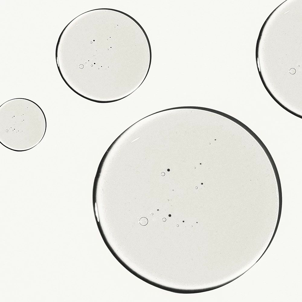 Diverse gocce rotonde e trasparenti su sfondo bianco. Le gocce hanno un bordo scuro e contengono piccole bolle.