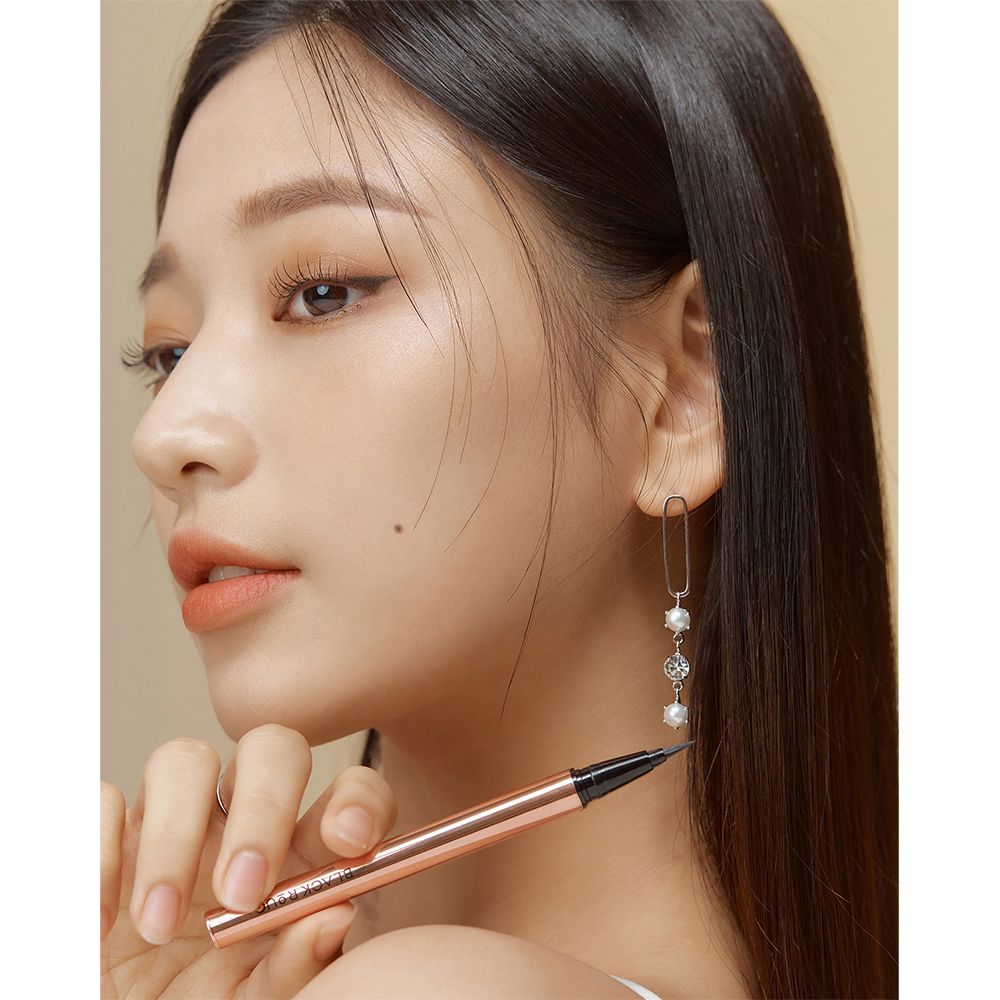 Una donna tiene in mano un eyeliner nero. La penna ha un corpo dorato. Il testo BLACK ROUGE è visibile.