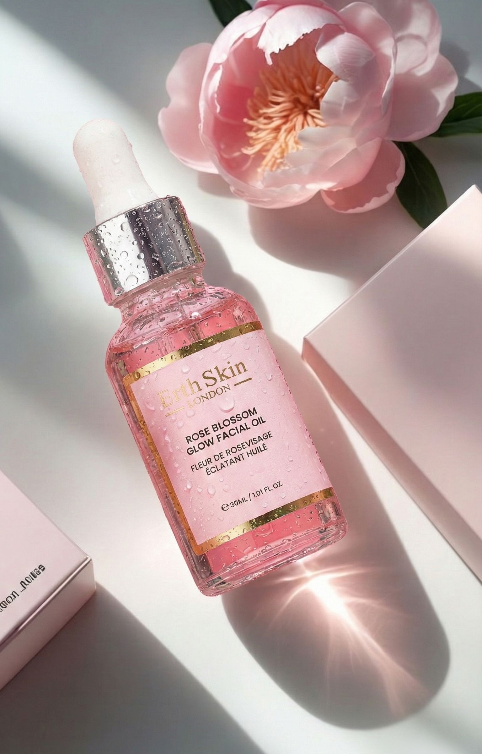 Flacone in vetro con contagocce, circondato da gocce d'acqua e fiori rosa. Contiene olio viso rosato.