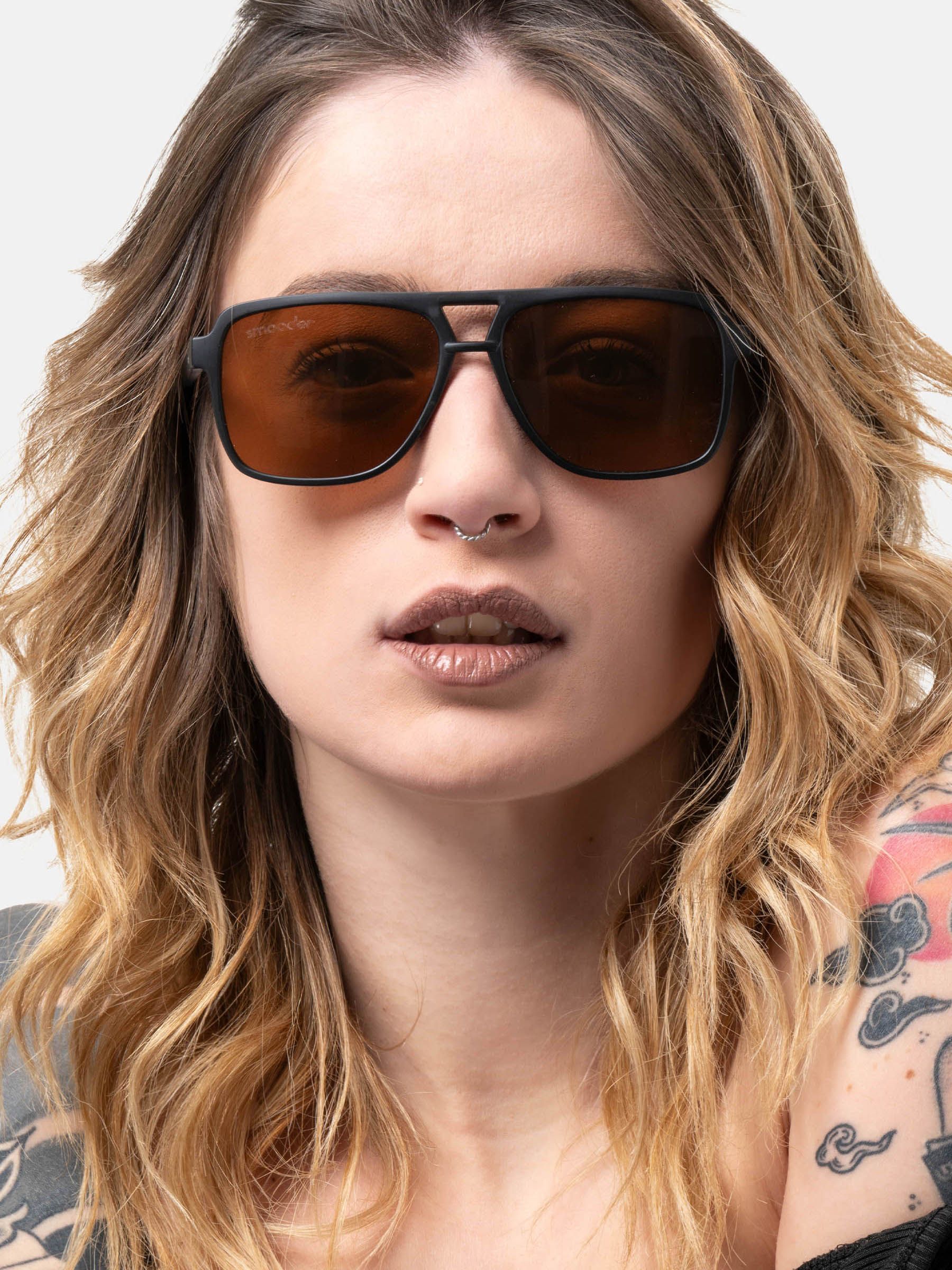 Una persona indossa occhiali da sole neri con lenti marroni. Il marchio "smooder" è visibile.