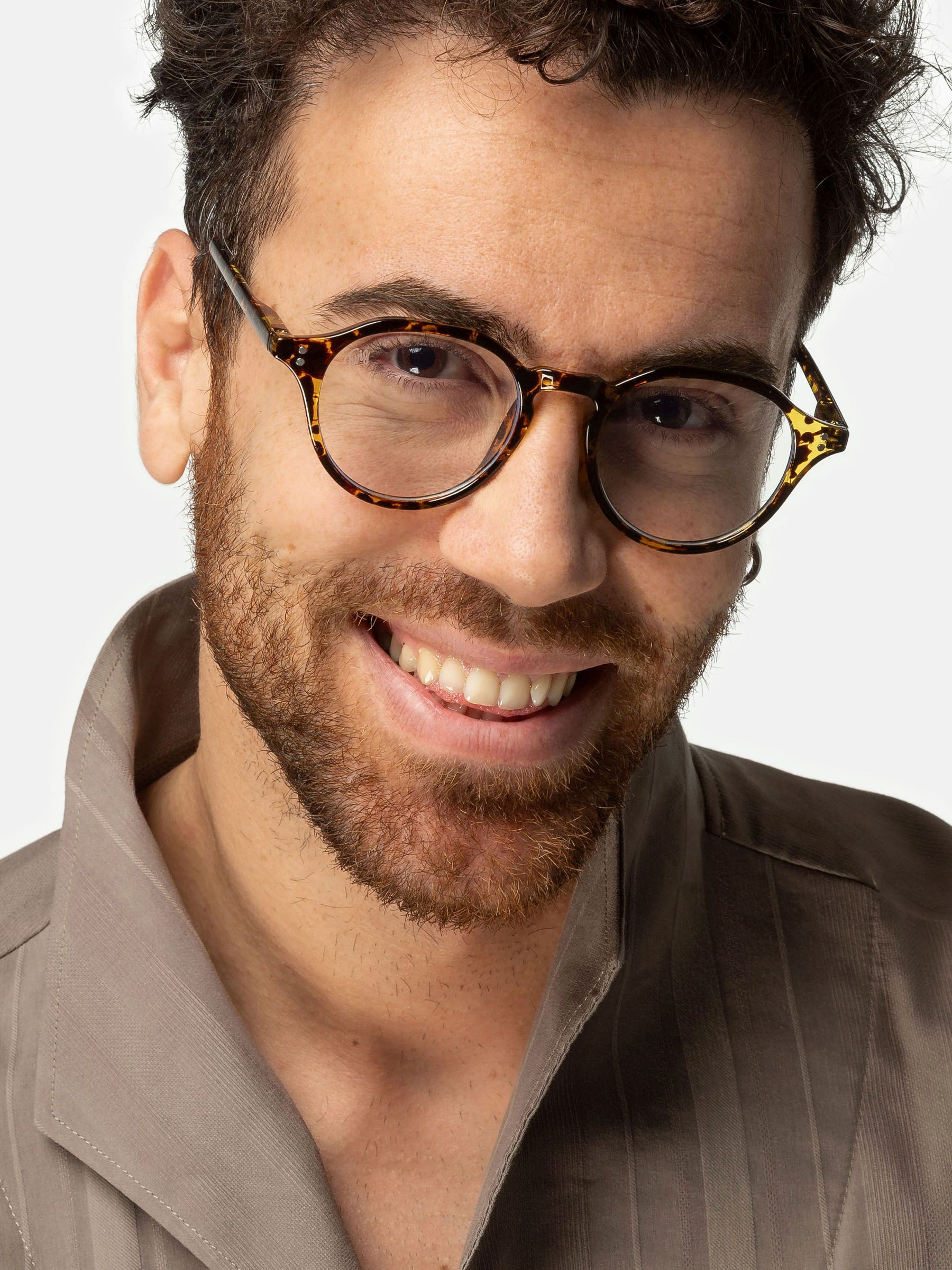 Uomo con occhiali. Lenti rotonde, motivo leopardato marrone. Sorride. Camicia beige.