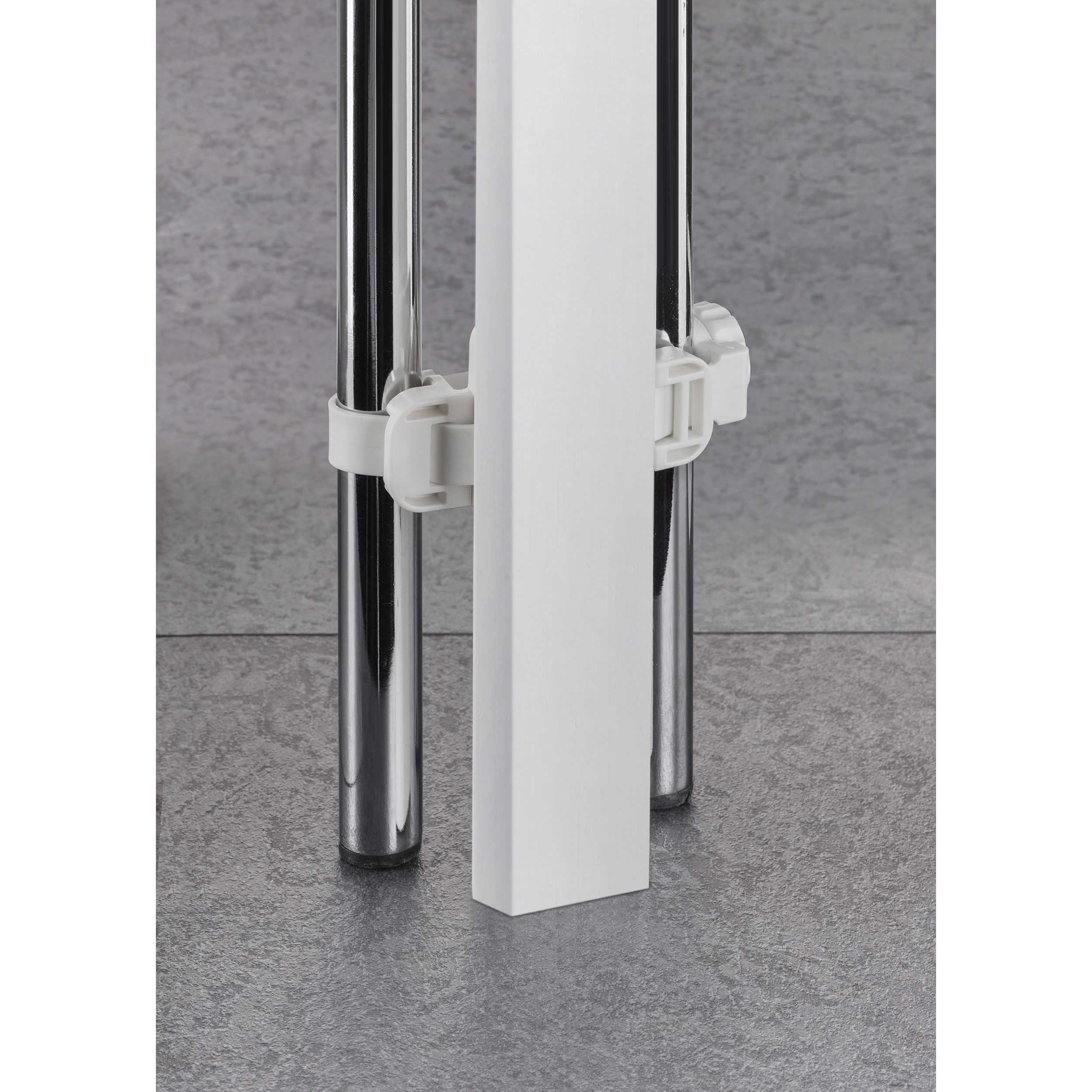 Elemento rettangolare bianco con due supporti bianchi, fissato a due tubi metallici. Pavimento grigio.