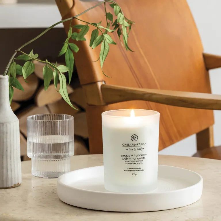 Candela Chesapeake Bay accesa, mind & body, peace + tranquility. Su piatto bianco. Vicino vetro e decorazioni.