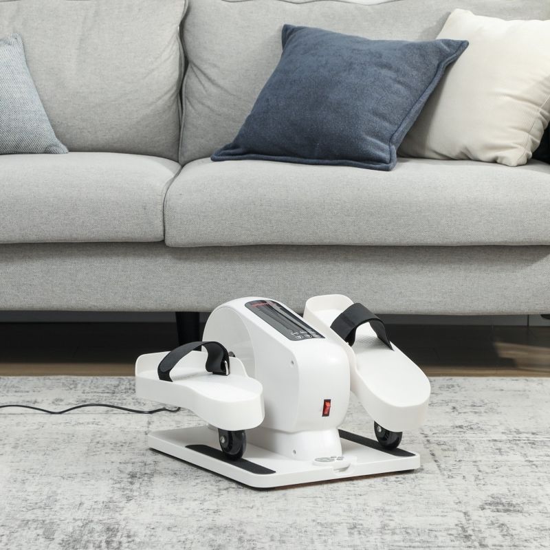 Mini ellittica bianca, cinghie nere. Su tappeto, davanti al divano. Pulsante on/off rosso, ruote.