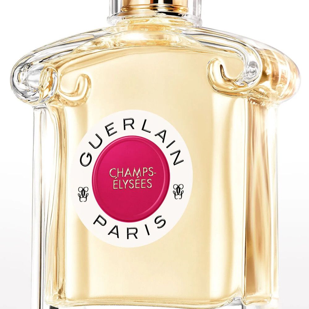 Flacone di profumo con etichetta rotonda. L'etichetta riporta "GUERLAIN PARIS" e "CHAMPS-ÉLYSÉES". Il flacone è in vetro.