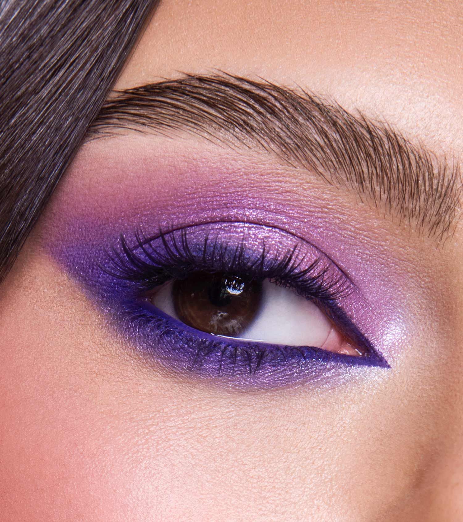Un occhio con ombretto e eyeliner viola scintillante e drammatico.