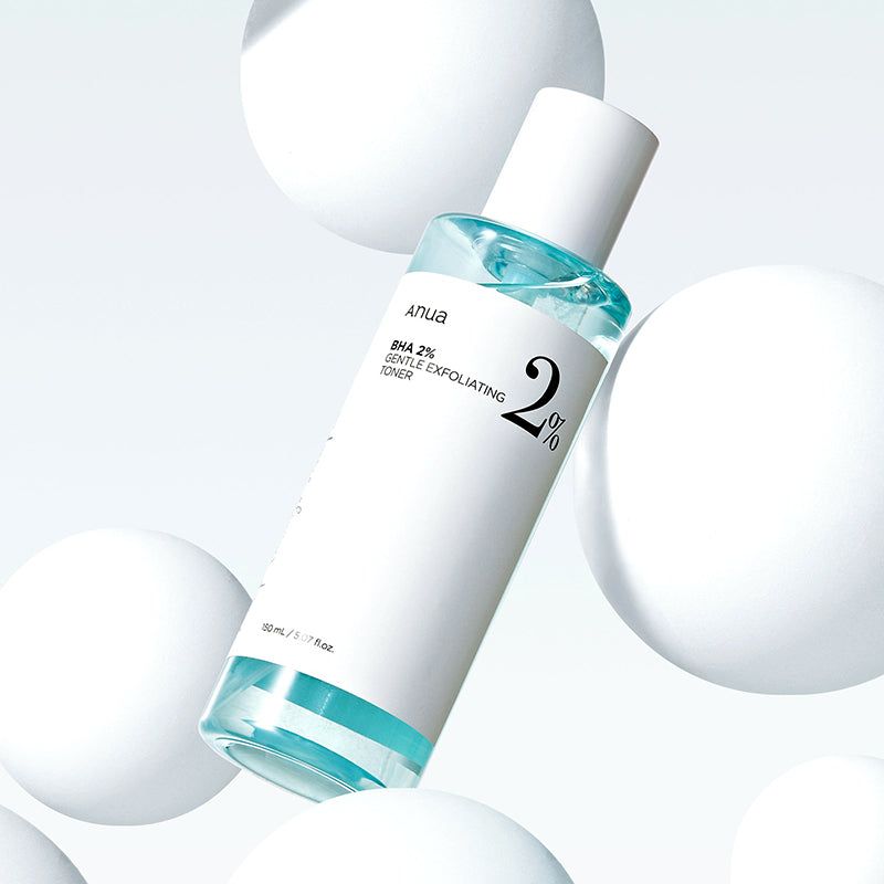 Flacone di toner con etichetta bianca e liquido blu, circondato da sfere bianche. Scritta: Anua BHA 2% Gentle Exfoliating Toner.