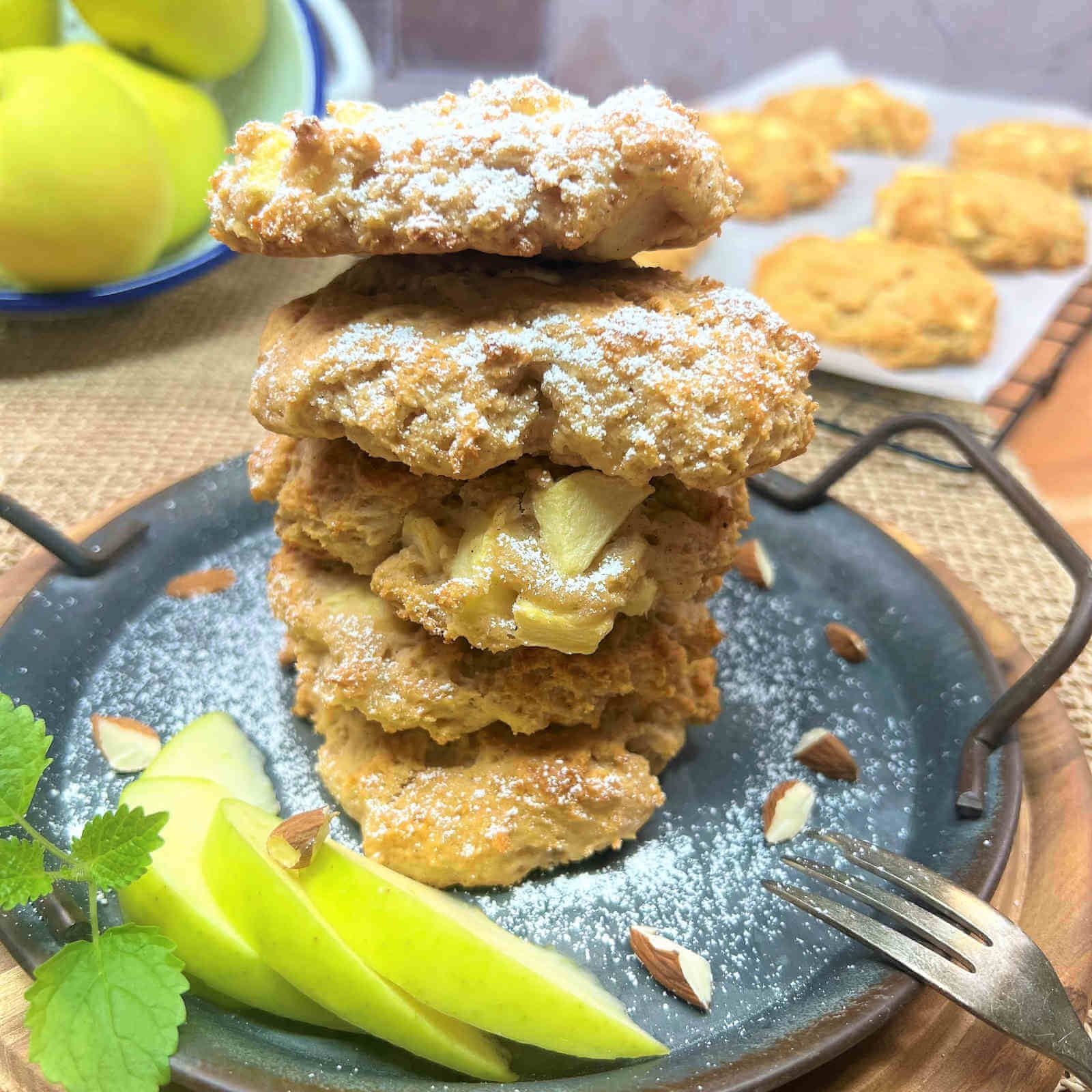 Biscotti impilati, spolverati di zucchero a velo, con pezzi di mela. Decorato su un vassoio con mandorle e fette di mela.
