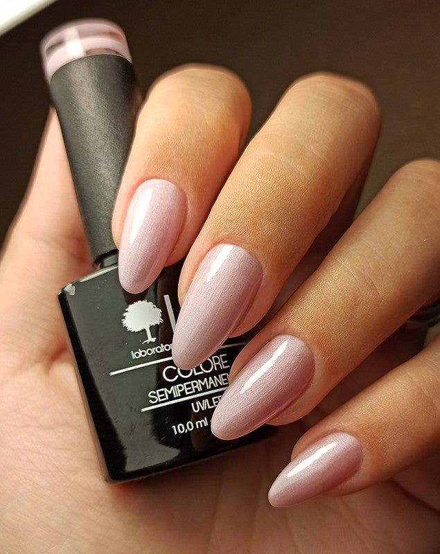 Mano con unghie smaltate e flacone di smalto. Unghie smaltate di rosa. Flacone nero, testo: LCI, Colore Semipermanente.