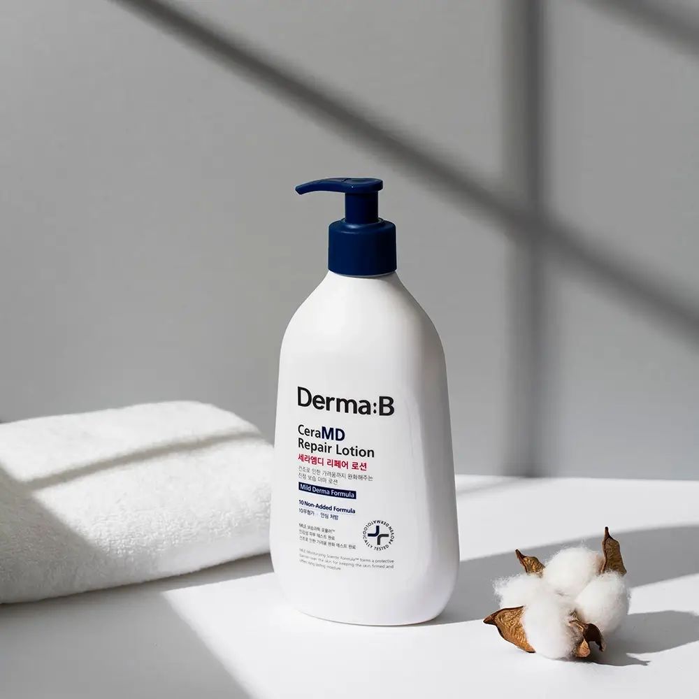 Flacone bianco con erogatore blu. Scritta: Derma:B CeraMD Repair Lotion. Accanto, un asciugamano e fiori di cotone.