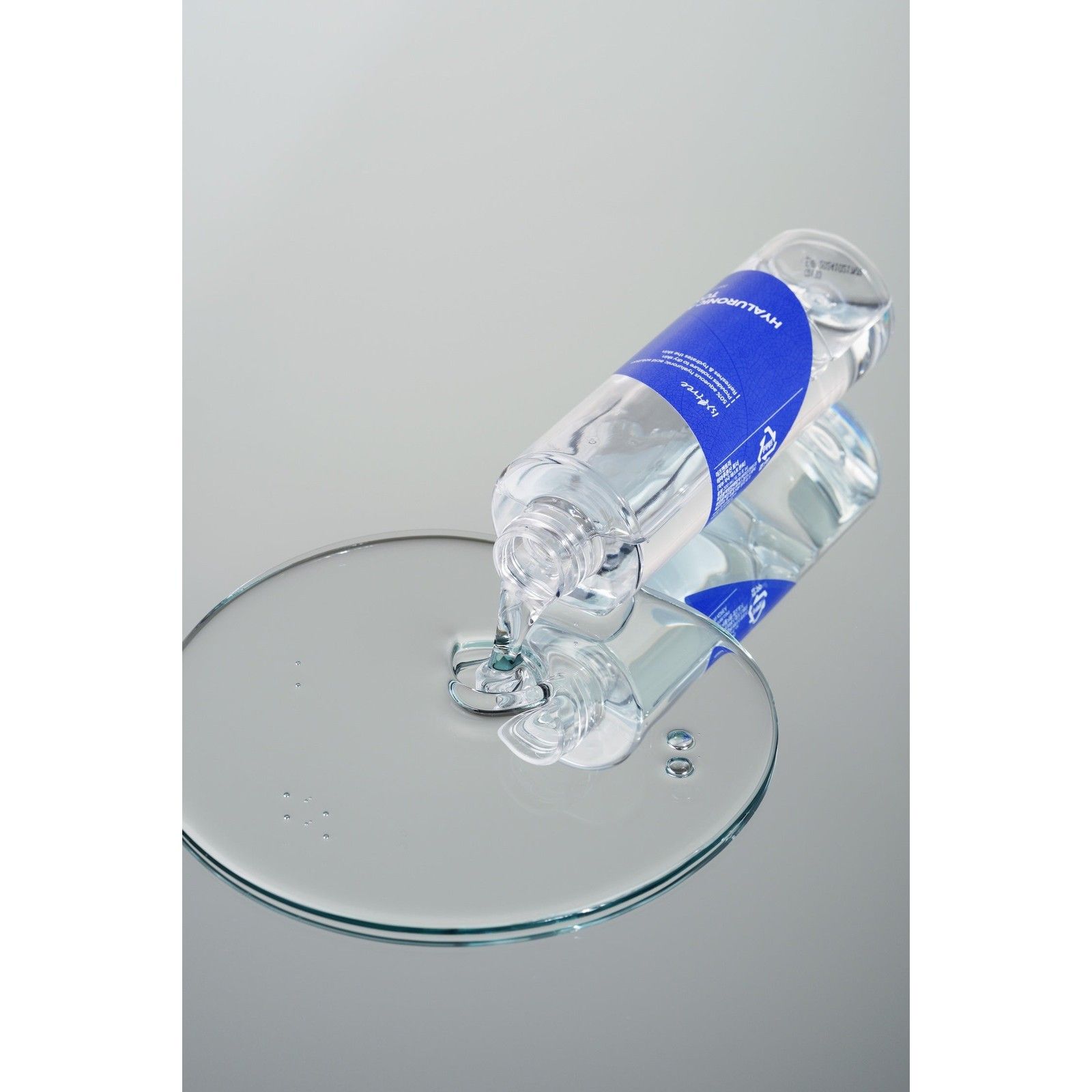 Isntree Hyaluronic Acid Toner cola da una bottiglia su una superficie riflettente, formando una grande goccia.