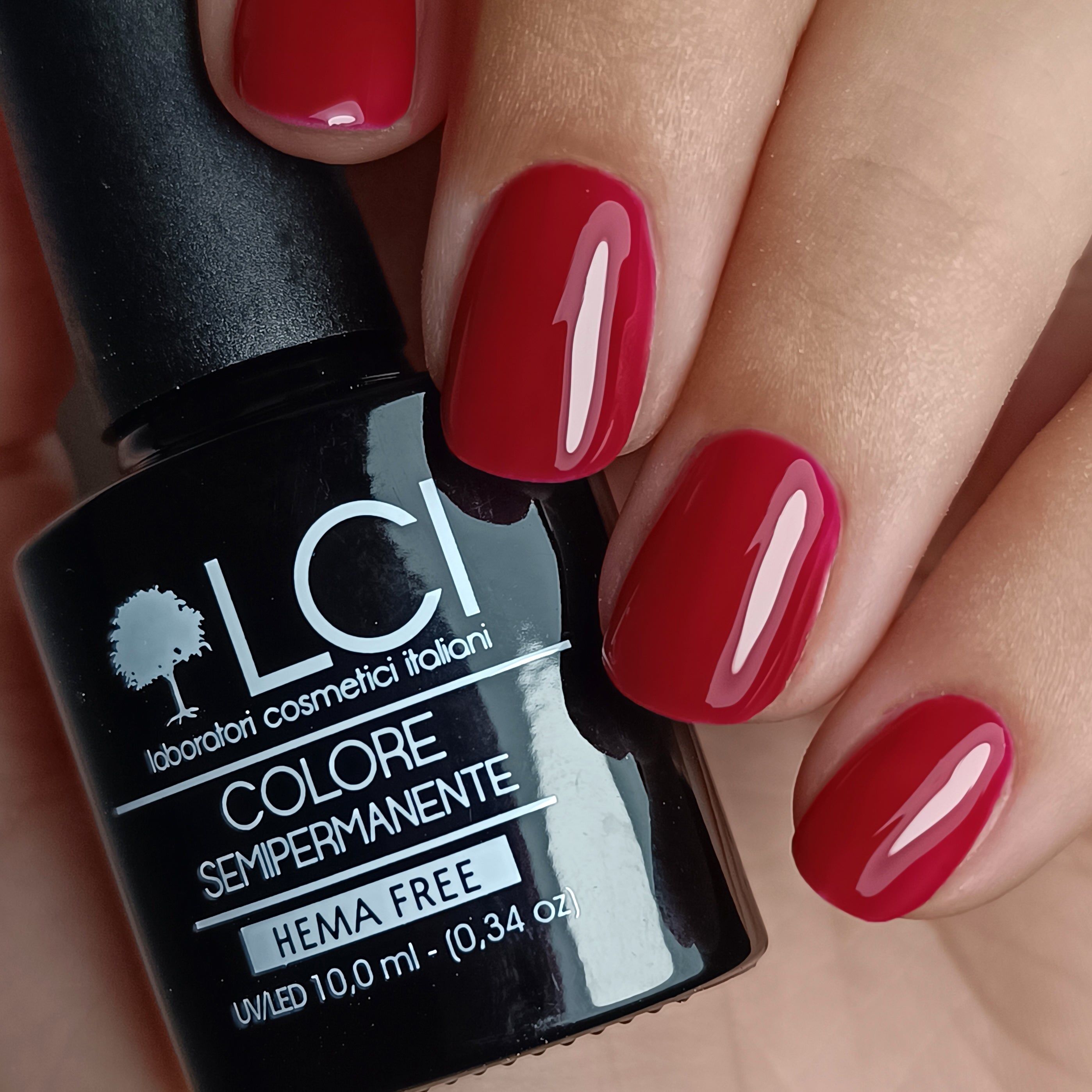 Flacone di smalto accanto a unghie smaltate. Flacone nero con scritta: LCI, Colore Semipermanente, HEMA FREE.