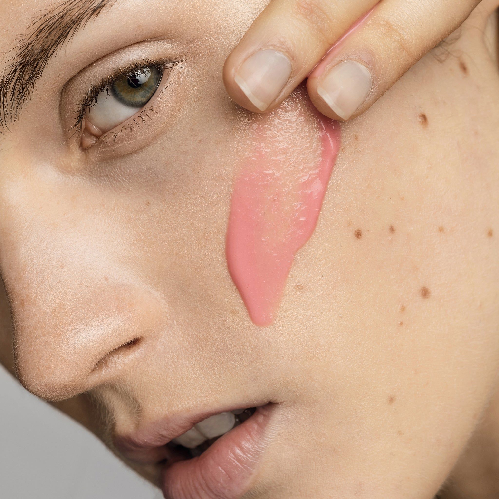 Primo piano di un viso. Siero rosa applicato sulla guancia. Pelle con lentiggini.