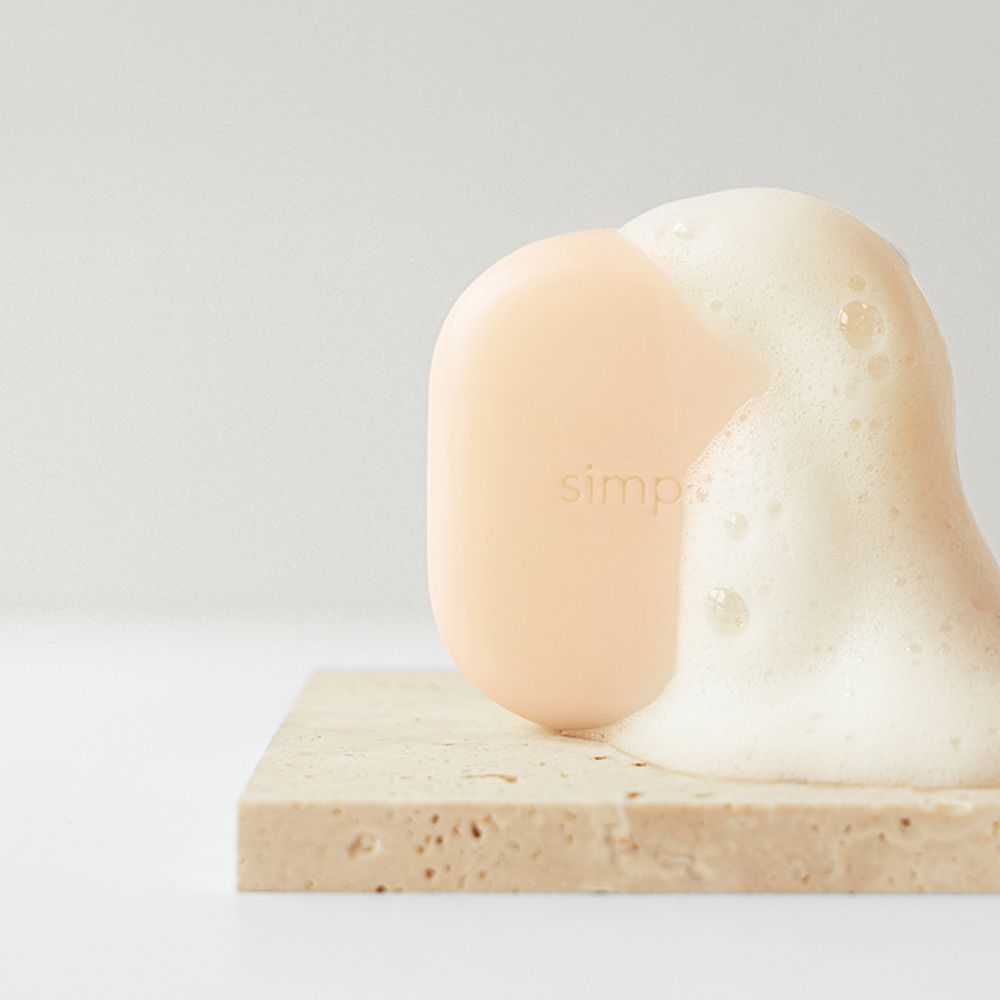 Barretta shampoo beige su lastra di pietra con schiuma. Logo visibile. Prodotto in uso.