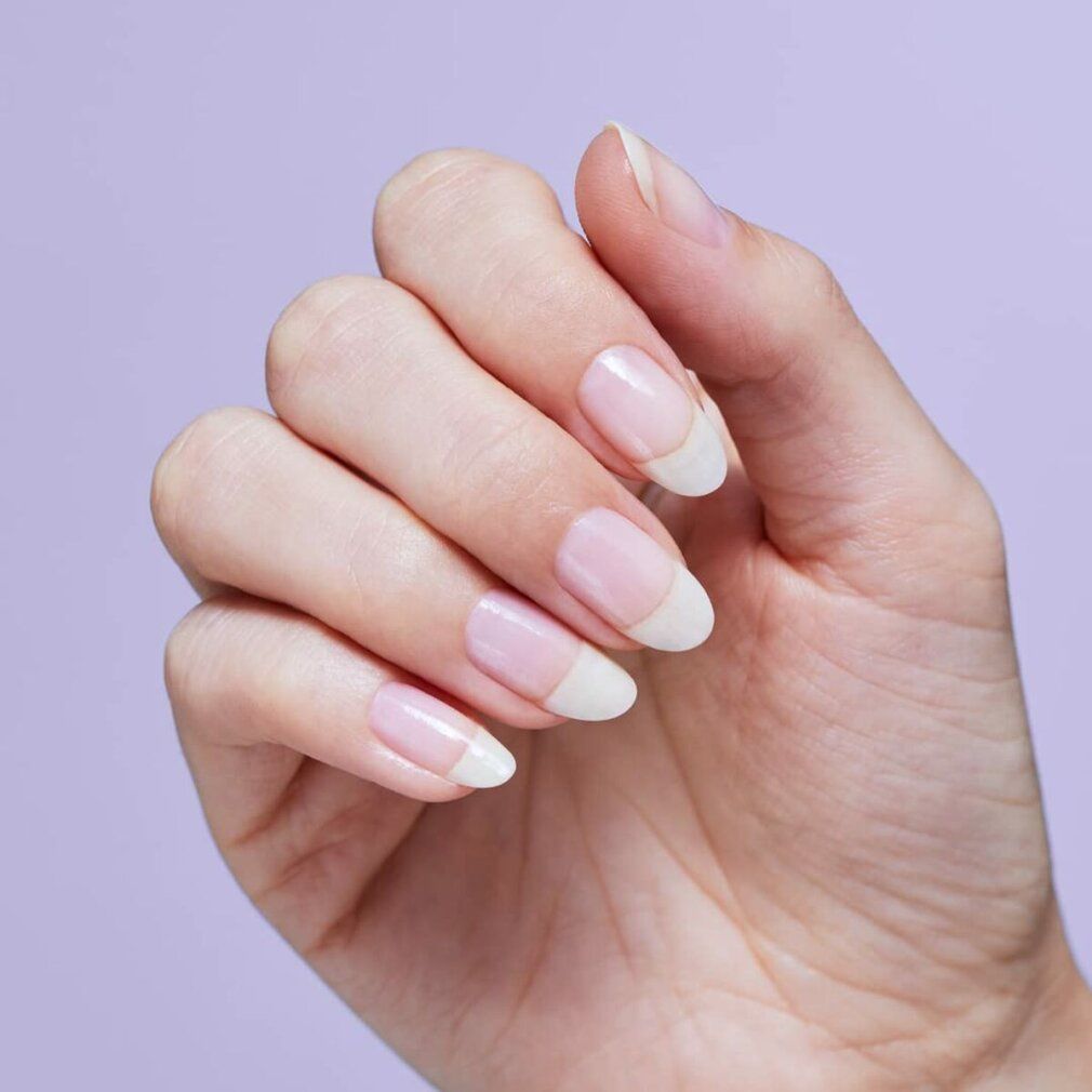 Mano con unghie alla francese. Le unghie sono ovali, con base rosa e punte bianche. Sfondo viola.