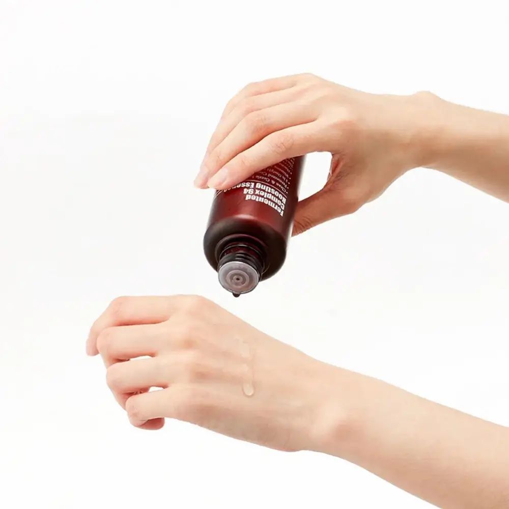 Flacone marrone, goccia sulla mano. Nome del prodotto non visibile. Il flacone è tenuto sopra la mano, cadono gocce.