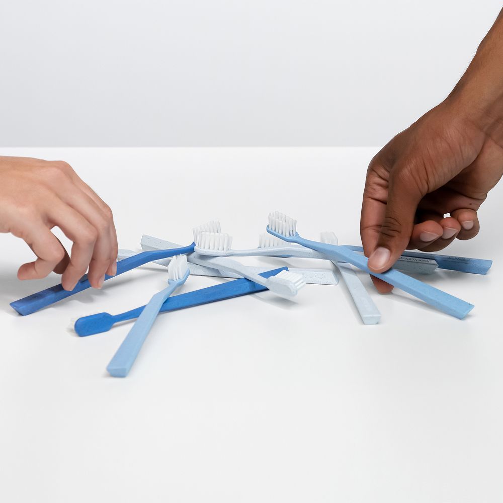 Diversi spazzolini blu su sfondo bianco. Mani che li afferrano.