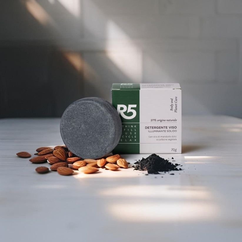 Detersivo viso solido grigio rotondo, con confezione e mandorle. Confezione con testo: R5, Detergente Viso Solido Illuminante.