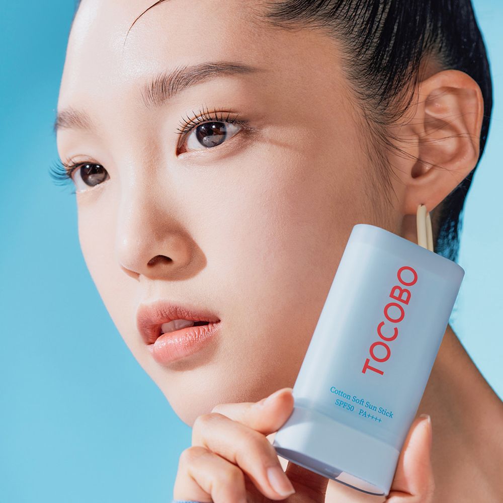 Ritratto di donna che tiene uno stick solare. Scritta TOCOBO in rosso. Testo: Cotton Soft Sun Stick SPF50+ PA++++.