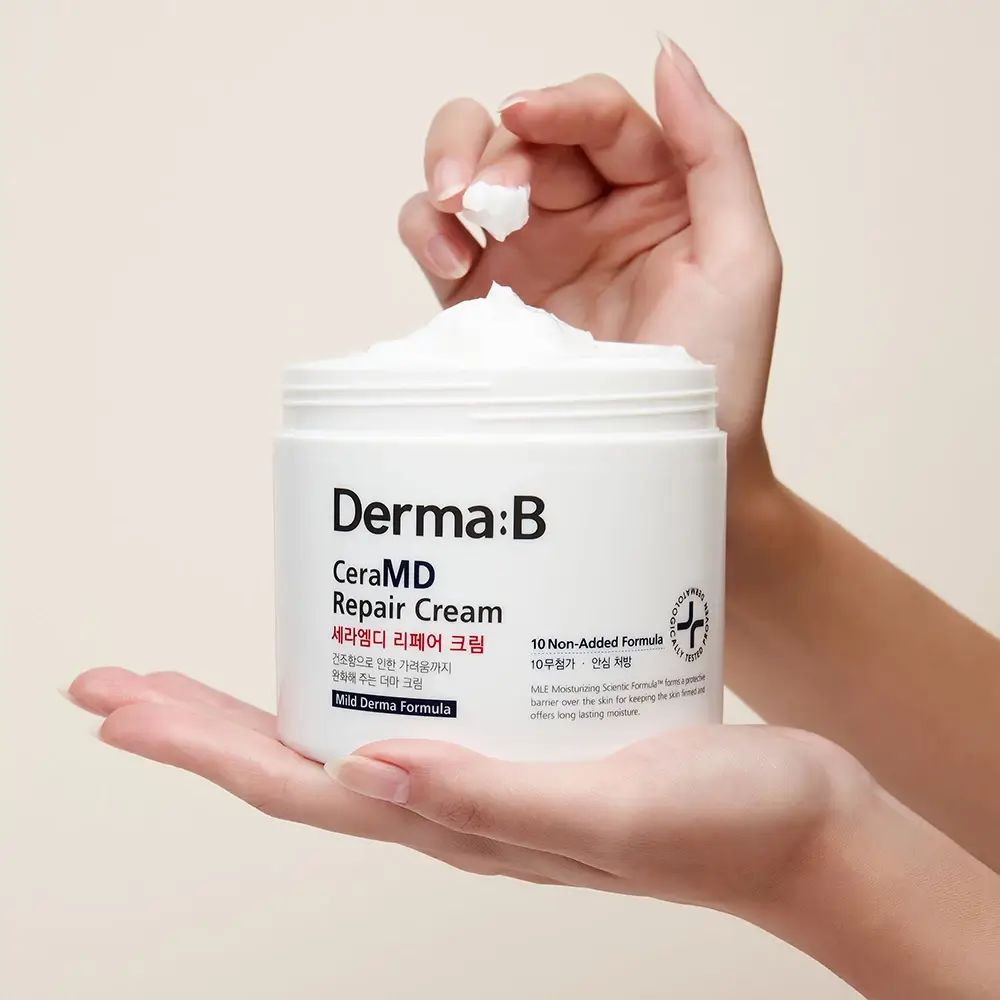 Mani che tengono un vasetto aperto di crema bianca. Scritta: Derma:B CeraMD Repair Cream.