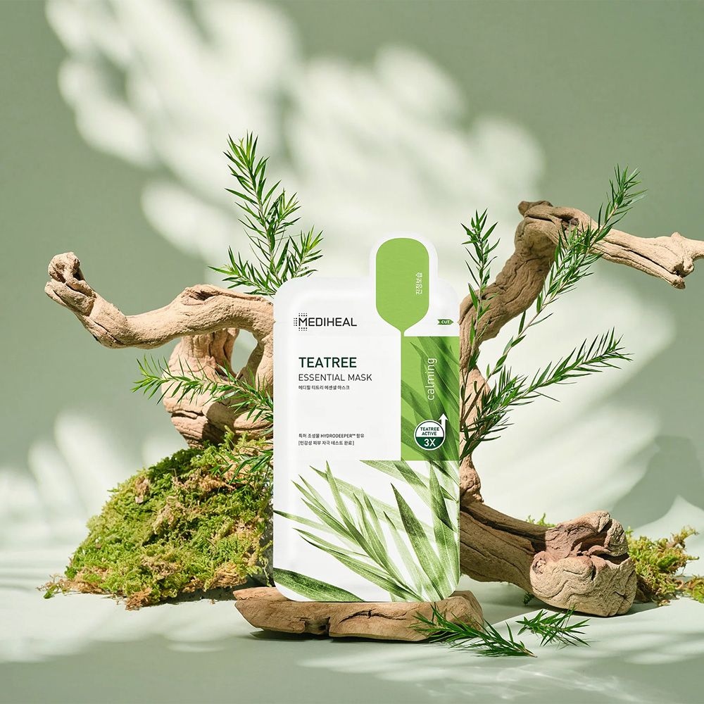 Confezione con maschera, circondata da legno e piante. Scritta: Tea Tree Essential Mask. Striscia verde con testo.