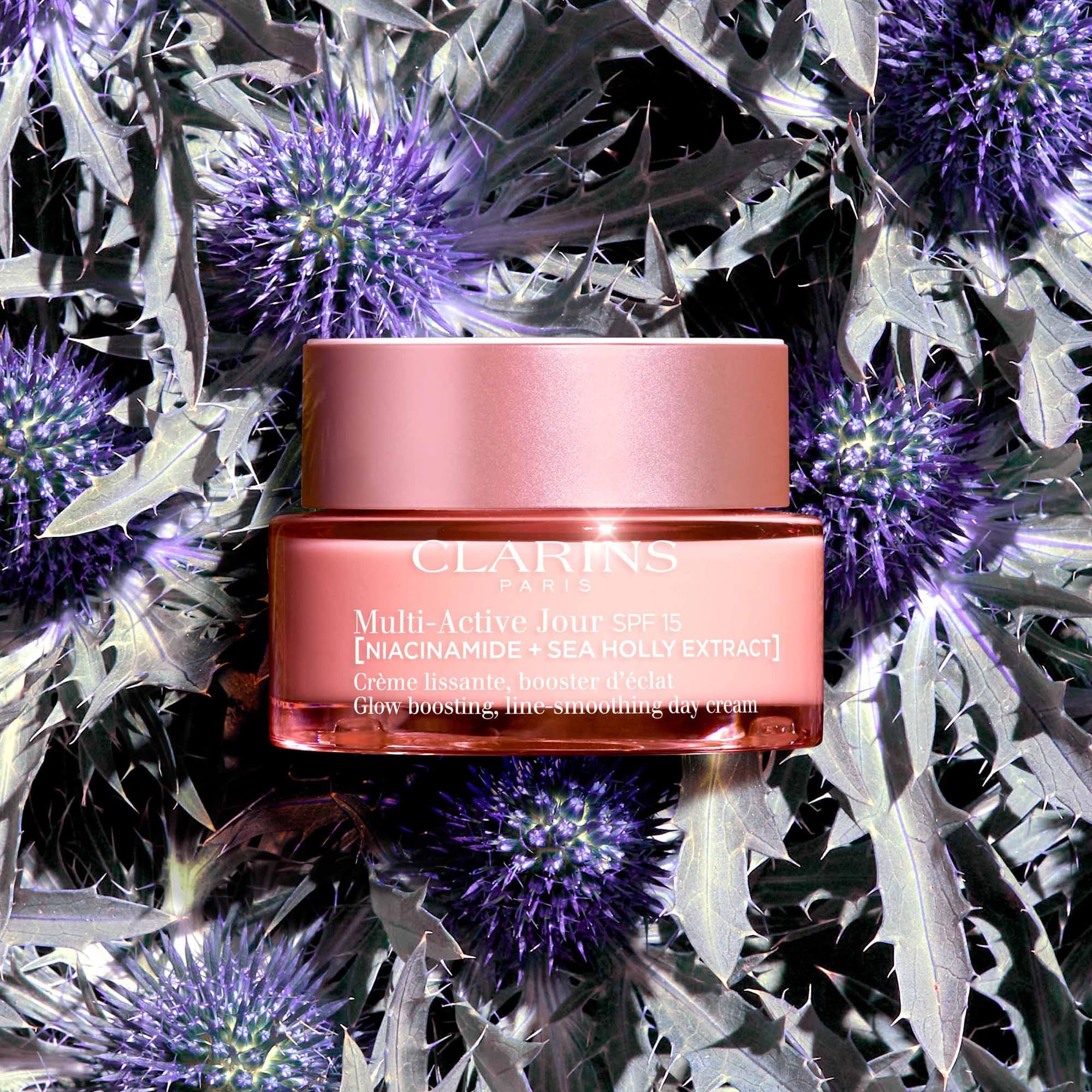 Vasetto di crema rosa con coperchio, circondato da fiori di cardo viola. Scritta: Clarins, Multi-Active Jour SPF15.