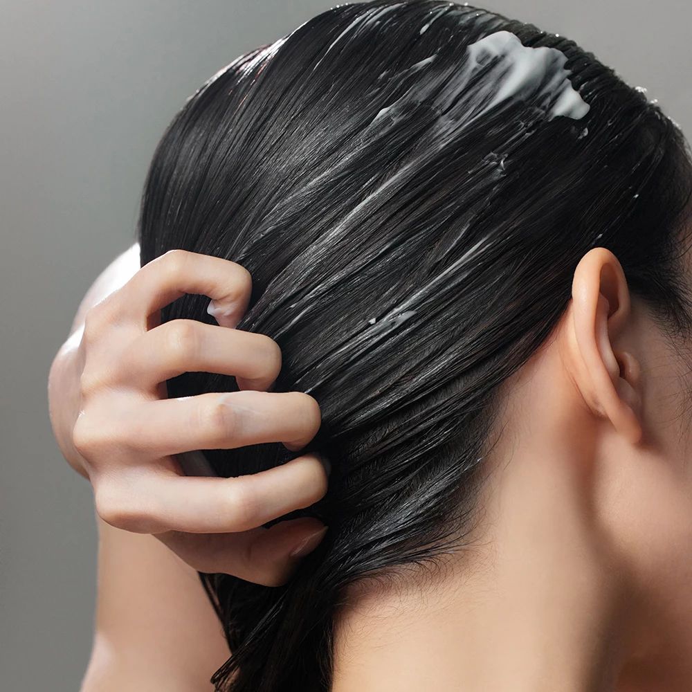 Persona che applica la crema sui capelli. Crema sui capelli. Visibili solo la nuca e la mano.