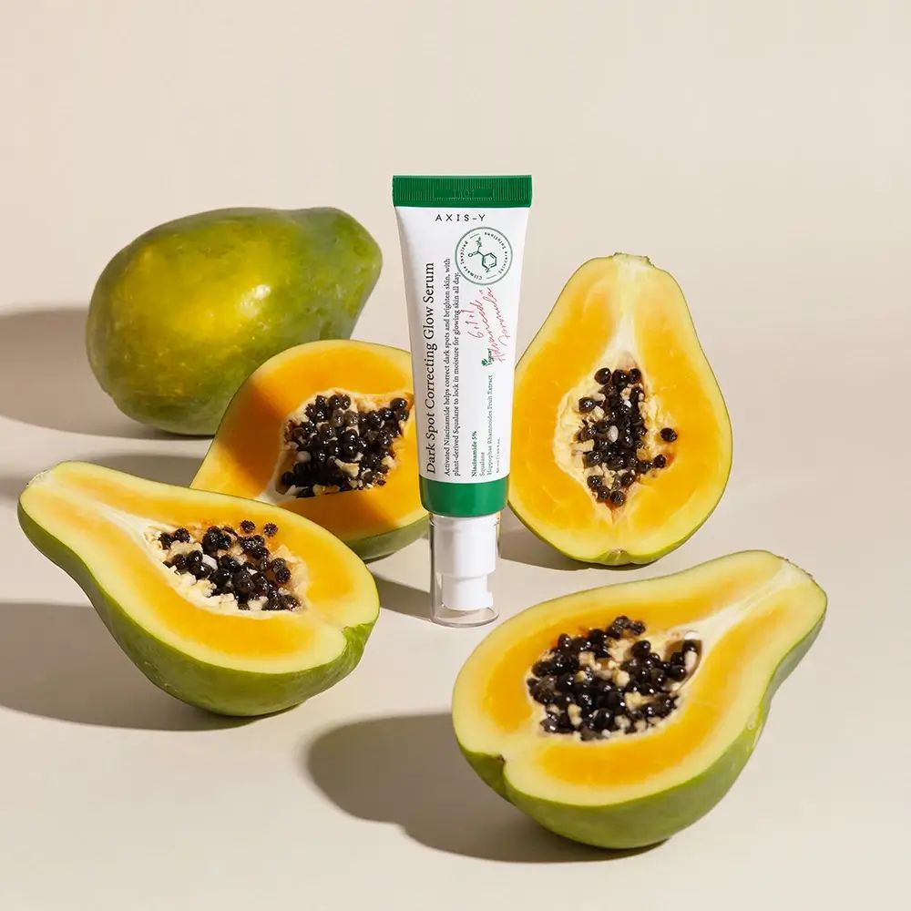 Prodotto e papaya. Scritta: Dark Spot Correcting Glow Serum. Marchio: AXIS-Y. Prodotto in tubetto bianco con tappo verde.