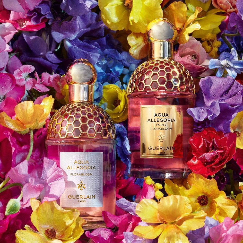 Due flaconi di vetro rosa con tappi dorati, circondati da fiori. Scritta: Aqua Allegoria Forte Florabloom, Guerlain.