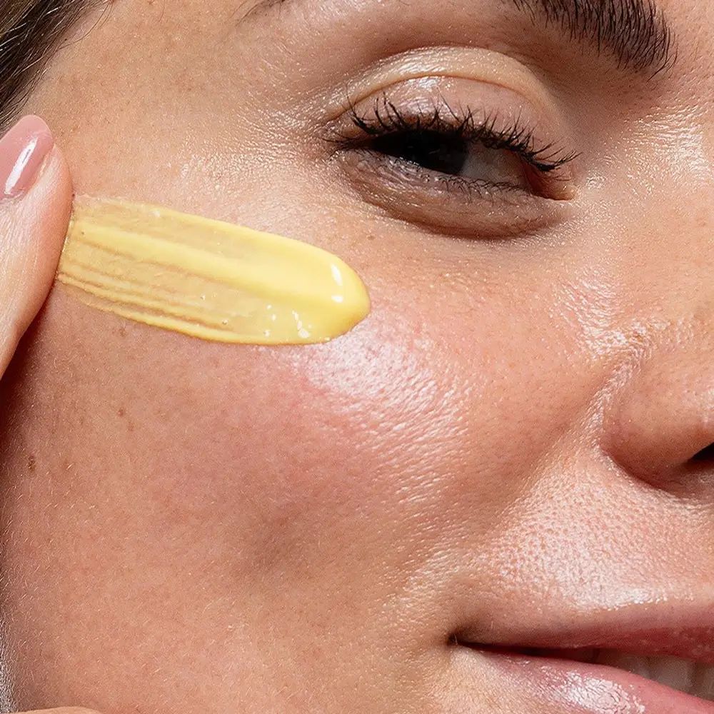 Primo piano di una donna che applica la crema sulla guancia. Crema gialla applicata.