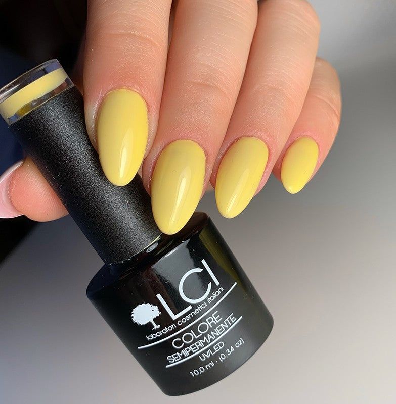 Mano con unghie smaltate e flacone di smalto. Unghie gialle e flacone di smalto nero con logo e testo bianchi.