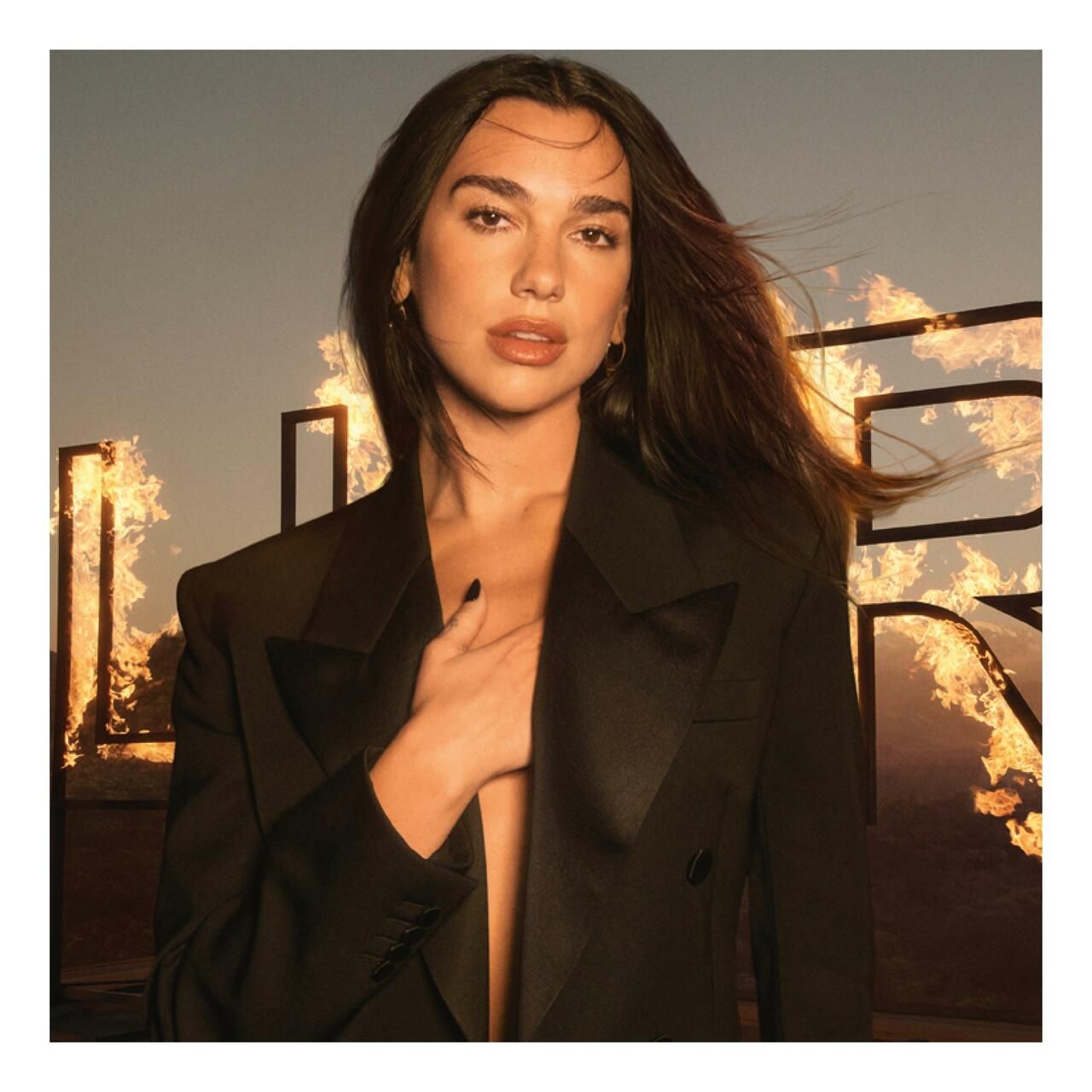 Ritratto di donna in blazer nero. Sfondo con fiamme e scritta. Donna con capelli scuri, sguardo verso la fotocamera.