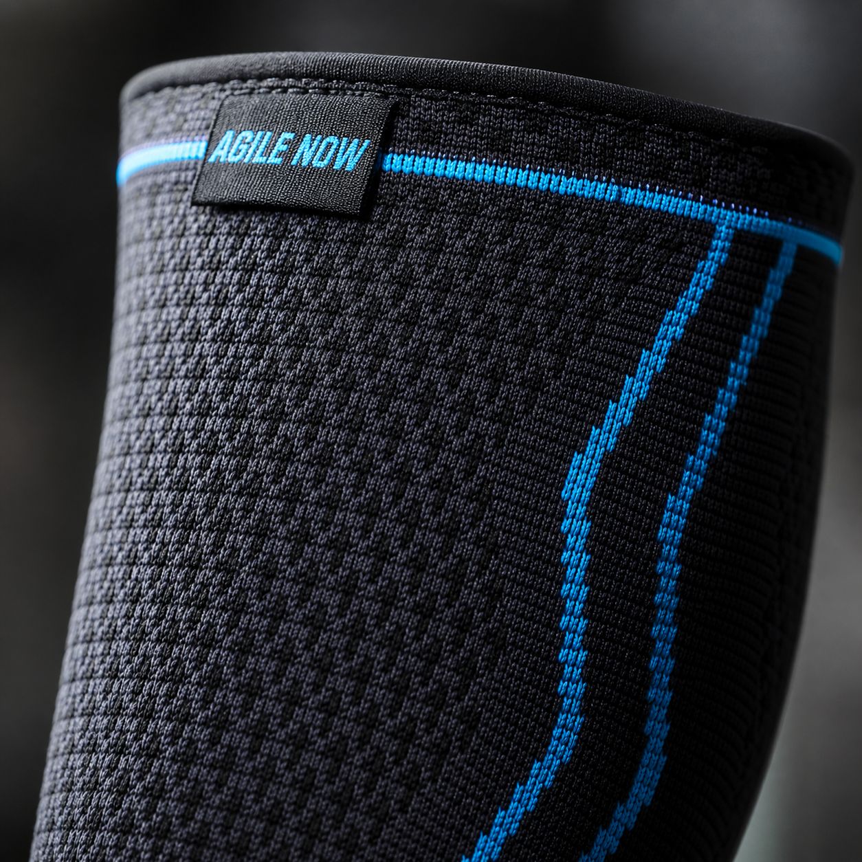 Primo piano di un bendaggio per polpaccio nero con linee blu e il testo AGILE NOW. Sfondo nero.