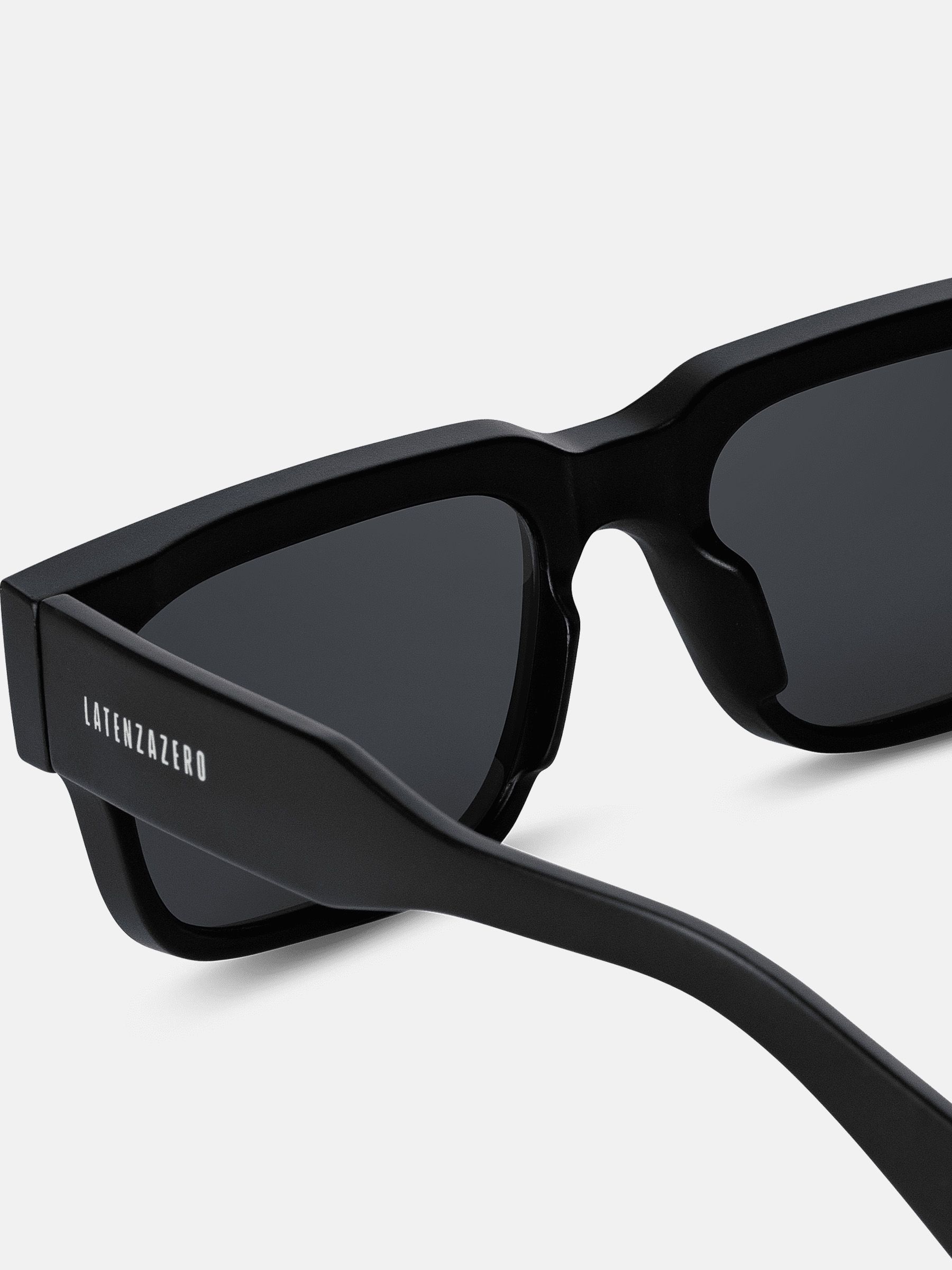 Primo piano degli occhiali da sole neri. Lenti rettangolari, logo sull'asta.