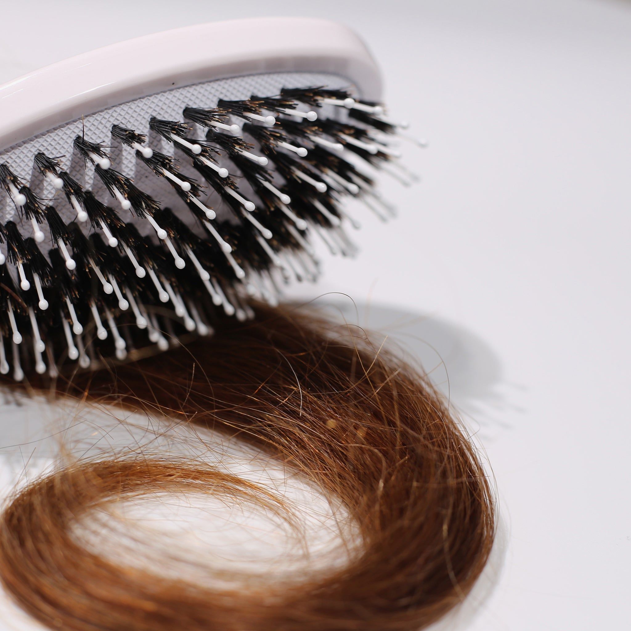 Primo piano di una spazzola bianca con setole nere e una ciocca di capelli.